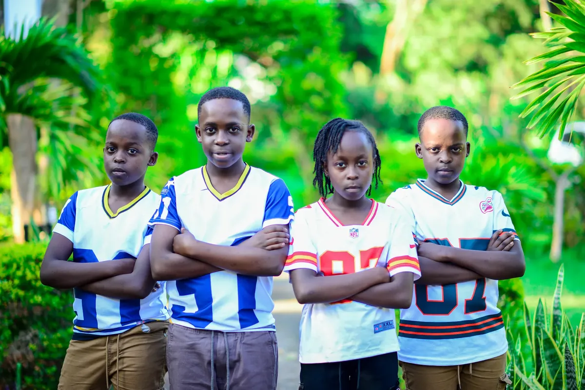 Group of four children posing confidently in sports jerseys, set in a lush outdoor environment.
