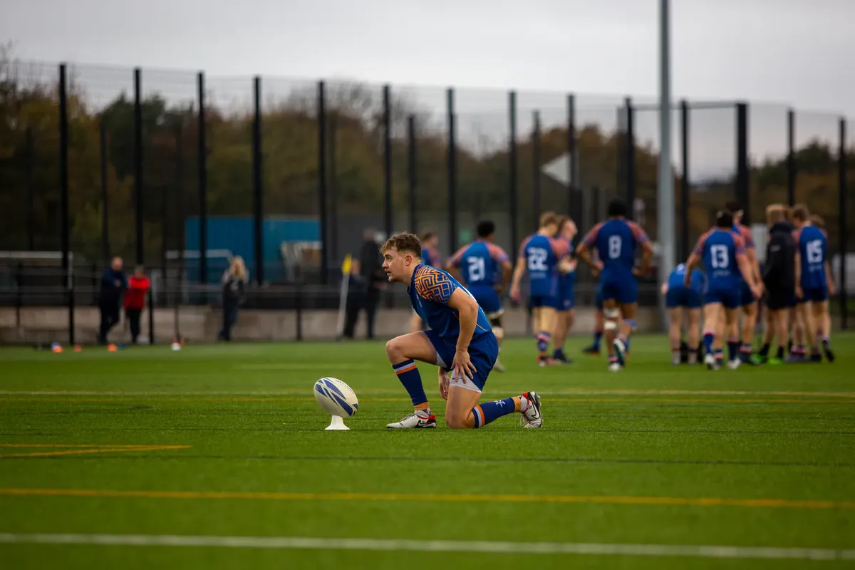 A rugby player prepares to kick the ball on a university field during a match.