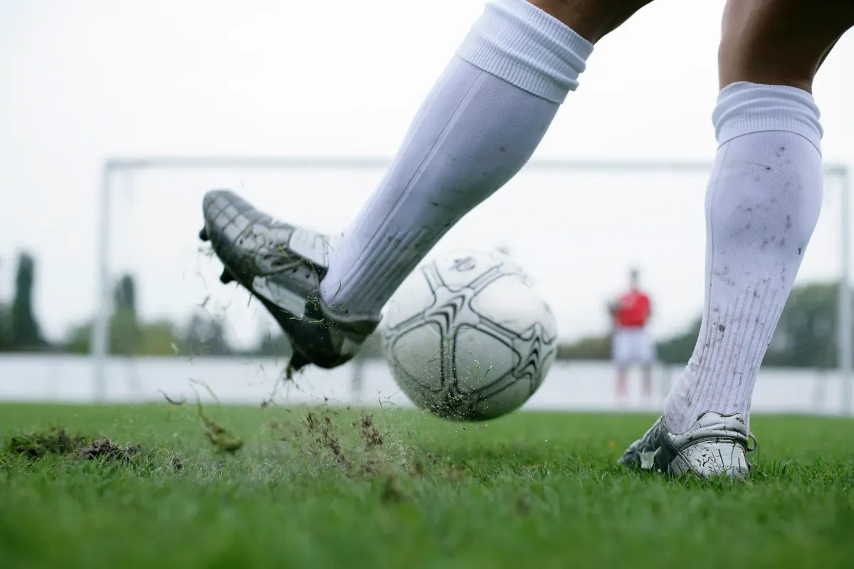 サッカー選手が芝場でボールを蹴るシーン。