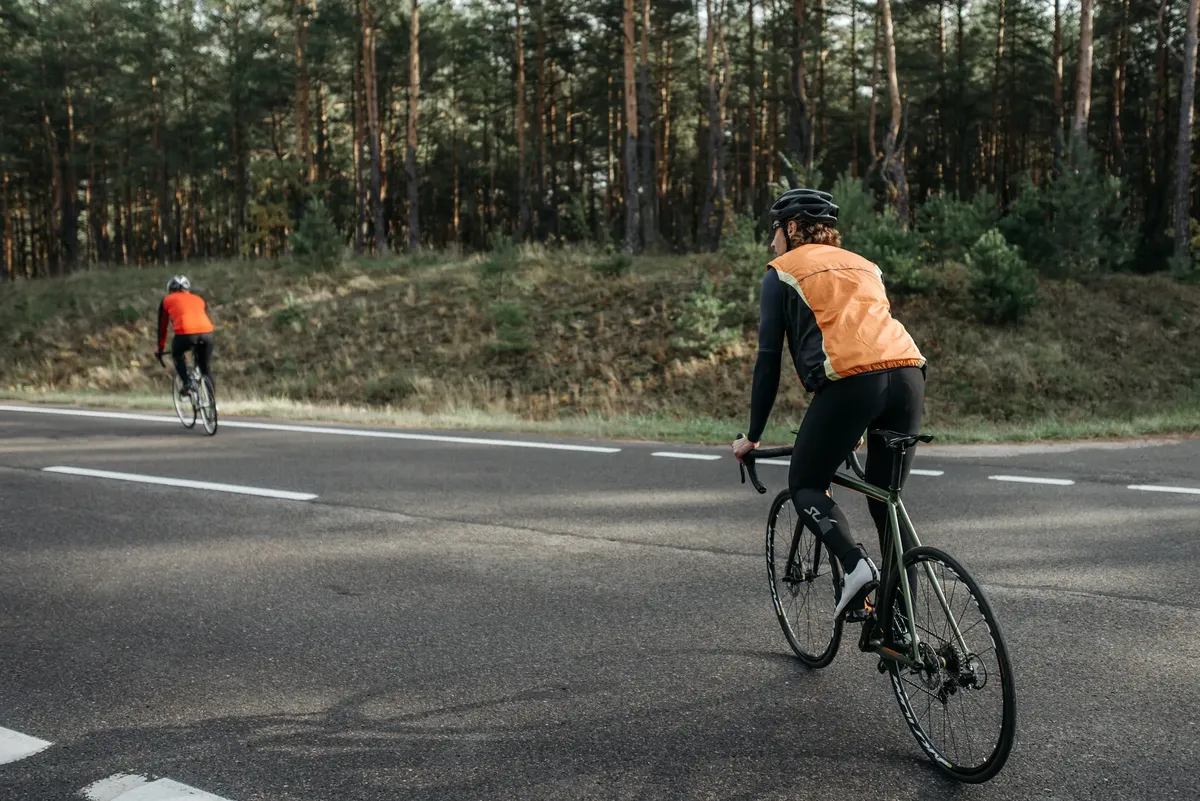 反射性のベストを着た2人の自転車乗りが森の道を進んでいる。自然とフィットネスを抱きしめる。
