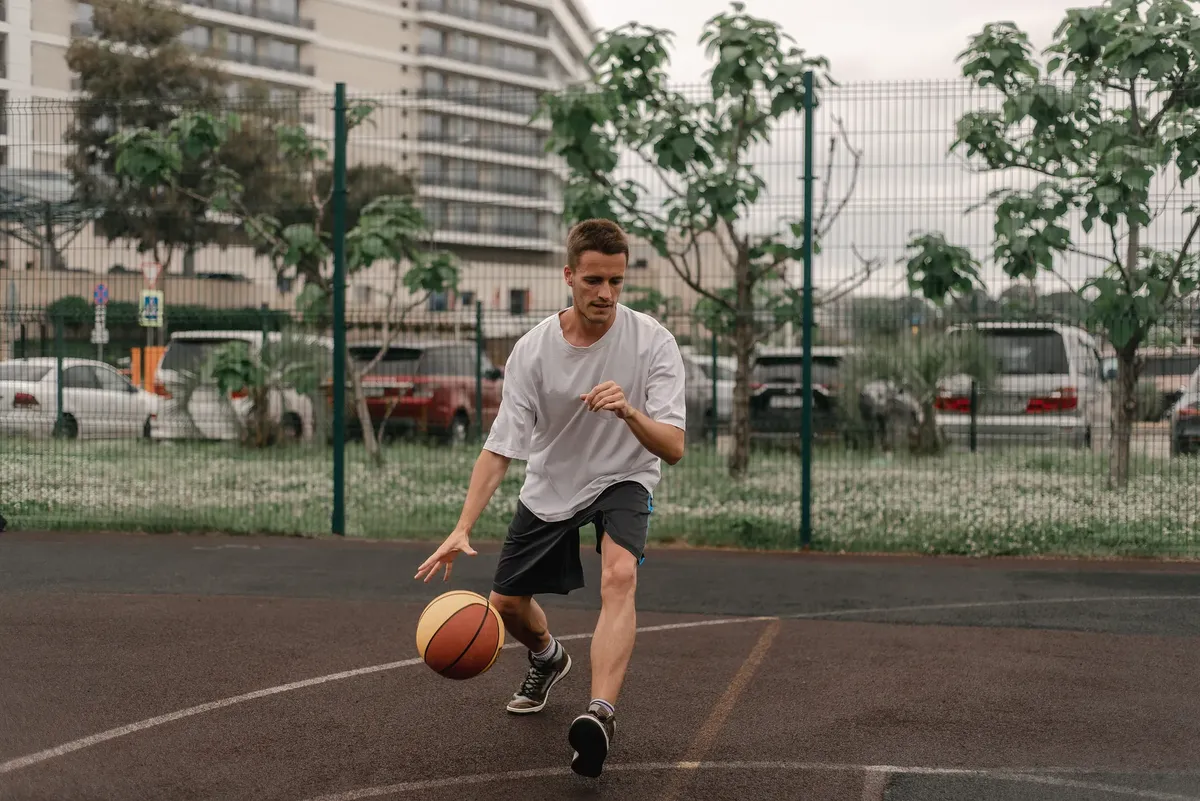 Young man skillfully dribbling a basketball on an outdoor court, showcasing sports agility.