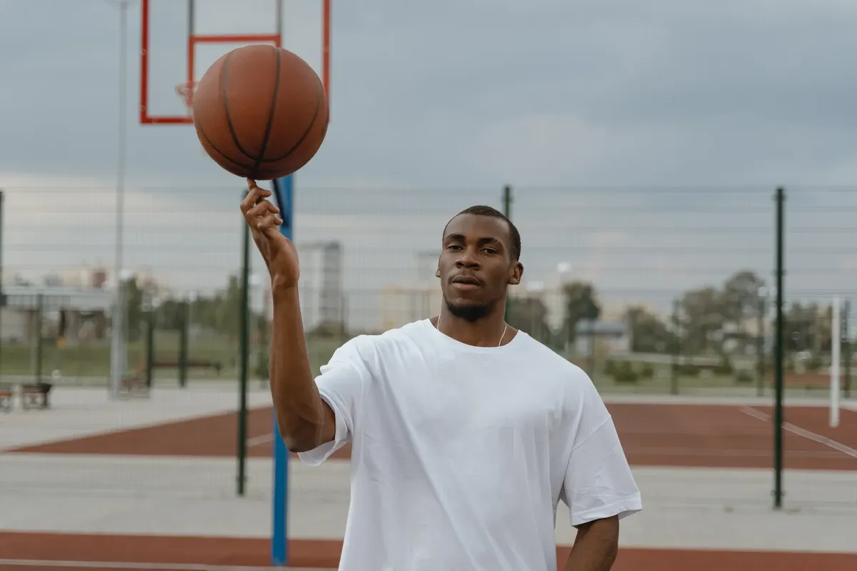 A young black man spins a basketball on his finger on an outdoor court, showcasing sports skills.