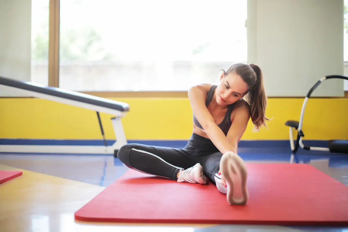 室内で柔軟性とフィットネスを強調する女性アスリートがヨガマット上でストレッチしている。