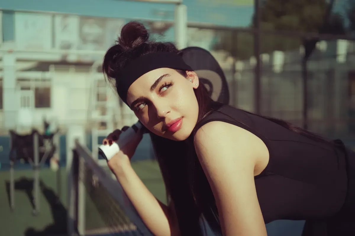 A young woman in sportswear prepares for a tennis match on an outdoor court, capturing a moment of focus and anticipation.