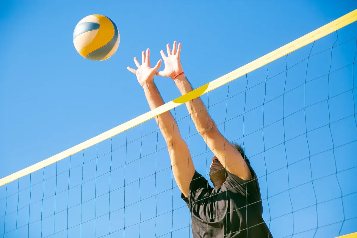 Dynamic outdoor volleyball game with a male player blocking a ball under clear blue skies.